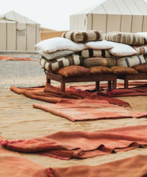 Detail of contemporary luxury glamping camp in Morocco Sahara desert.  Heap of many different pillows and red rug carpets.