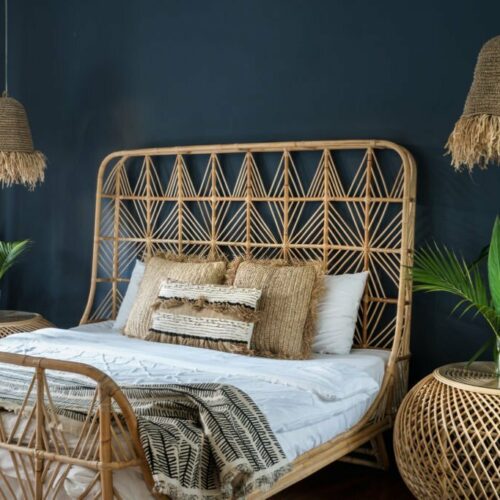Bohemian style interior at cozy house with ethnic decor. Elegant bedroom with lamps over bedside tables, pillows at comfortable bed, cactus plant and copy space on deep blue wall